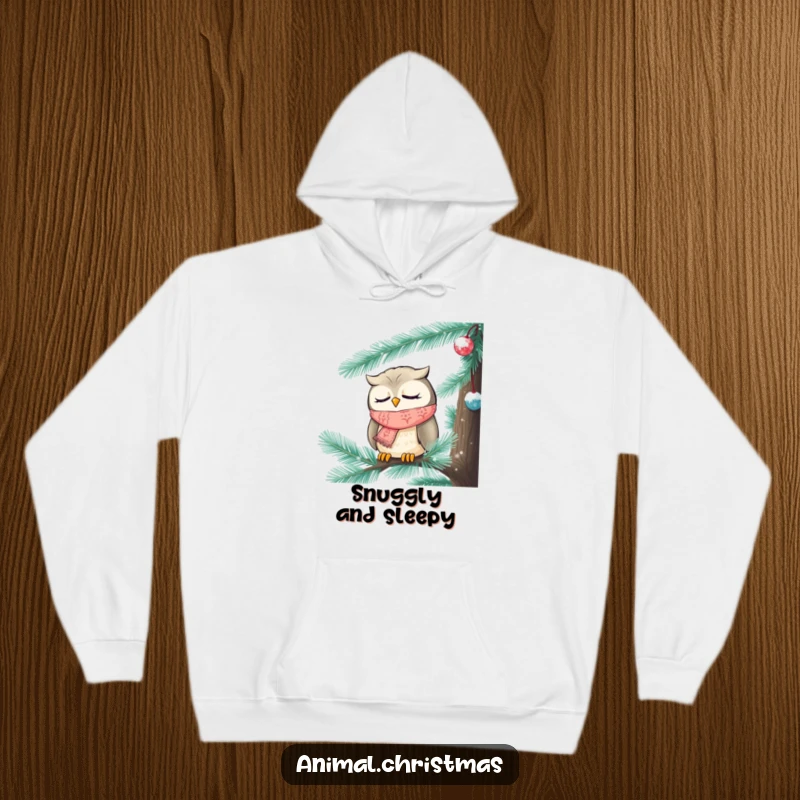 Funny Christmas hoodie showing a sweet, sleepy owl wearing a knitted scarf, tucked cozily inside a frosted pine tree.